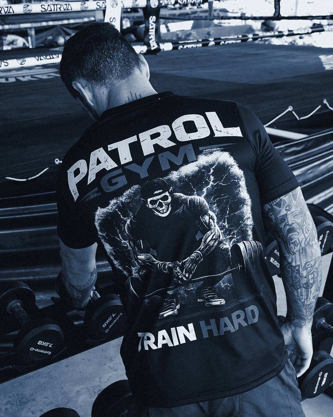 PatRol Gym feliratú mez hátulnézetből, mögötte kézisúlyzó-állvány